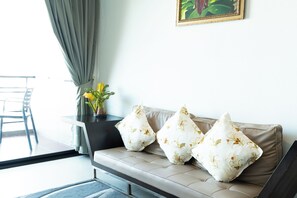 Un salon moderne avec un canapé beige, deux coussins à motifs, une petite table sur laquelle est posé un vase de fleurs et un tableau encadré accroché au mur.