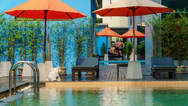 A pool area with lounge chairs and umbrellas, surrounded by plants and a blue wall. - The Vogue Hotel, Pattaya (Pattaya)