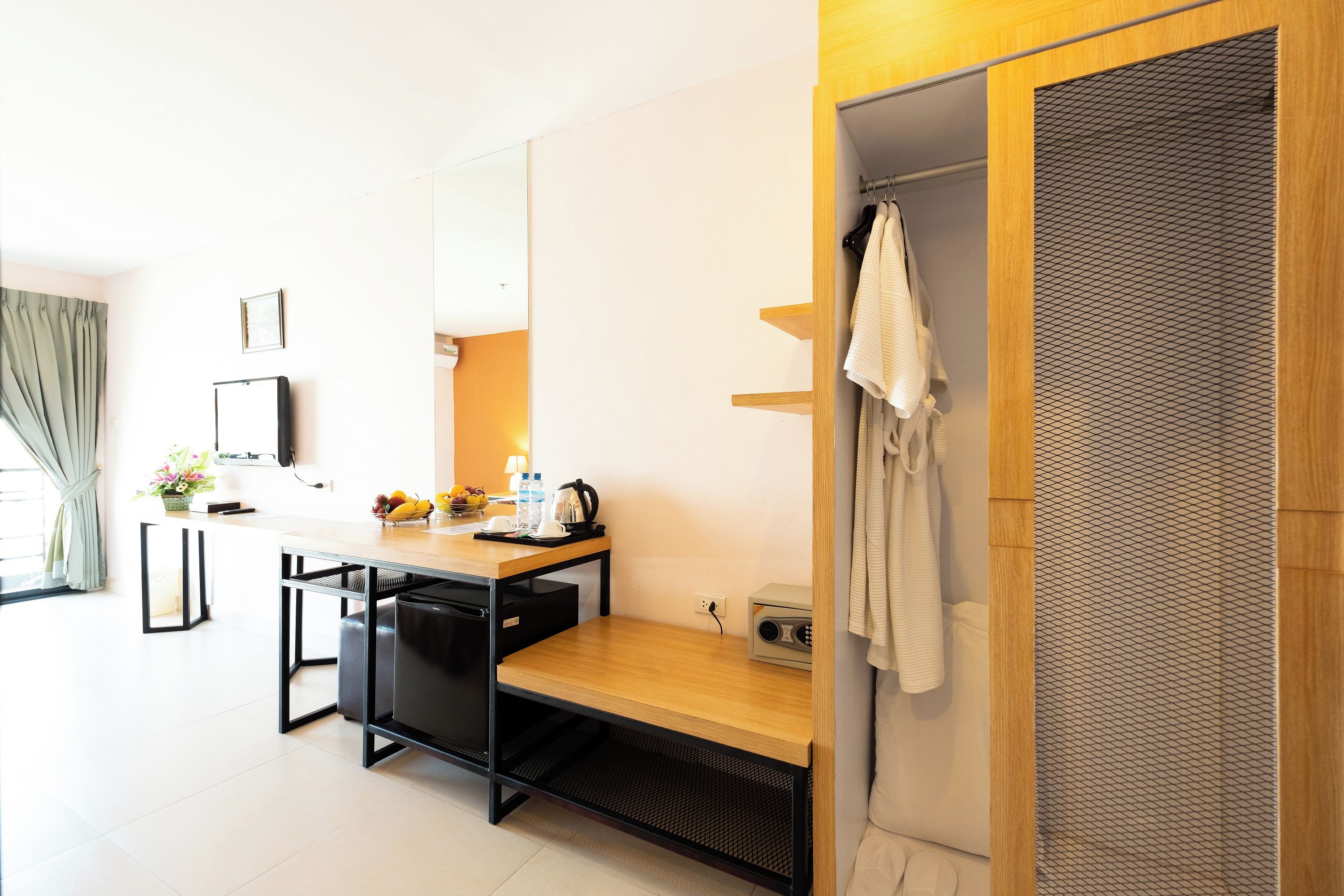 A modern hotel room with a wooden desk, a small kitchenette, a shower area, and a large mirror.