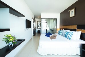 A modern hotel room with a large bed, a flat-screen TV, a vase of flowers, and a view into the bathroom. - The Vogue Hotel, Pattaya (Pattaya)