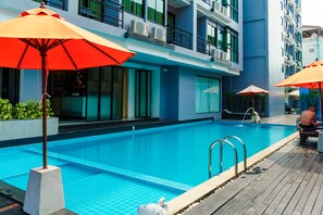 A modern hotel pool area with clear blue water, a wooden deck, and orange umbrellas. - The Vogue Hotel, Pattaya (Pattaya)