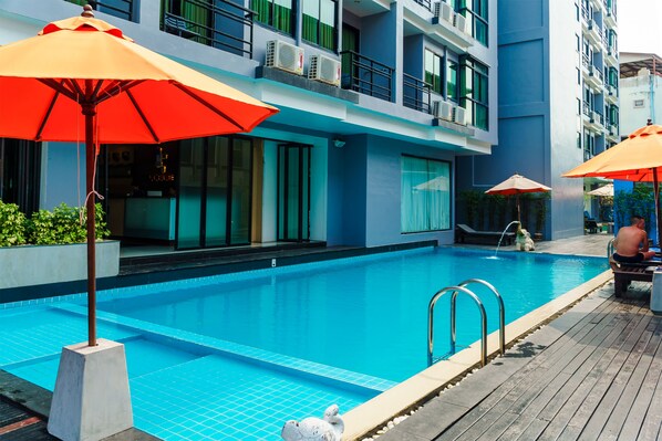 A modern hotel pool area with clear blue water, a wooden deck, and orange umbrellas. - The Vogue Hotel, Pattaya (Pattaya)