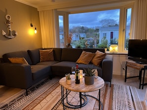 Ein modernes Wohnzimmer mit einem Ecksofa, einem runden Couchtisch und einem Flachbildfernseher.