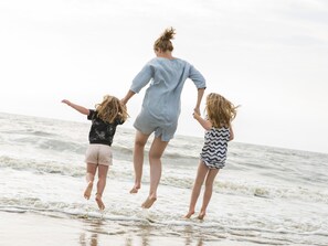 Eine Strandansicht mit einer Person und zwei Kindern, die in die Luft springen.