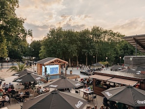 Ein Außenbereich mit Sitzgelegenheiten, Sonnenschirmen, einer Bühne und einer Snackbar.