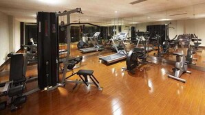 A gym with various exercise equipment, including treadmills and weight machines, arranged on a wooden floor with mirrors on the walls. - Hengshan Park (Beijing)