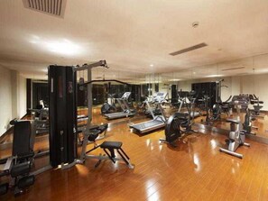 A gym with various exercise equipment, including treadmills and weight machines, arranged on a wooden floor with mirrors on the walls. - Hengshan Park (Beijing)