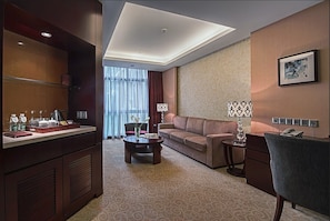 Une chambre d’hôtel équipée d’un canapé, d’une table basse, d’un bureau, d’une lampe et d’un mini-bar.