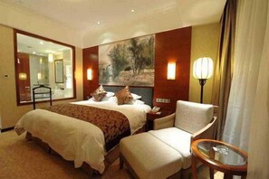 A hotel room with a large bed, a chair, a small table, a painting on the wall, and a lamp. - Hengshan Park (Beijing)