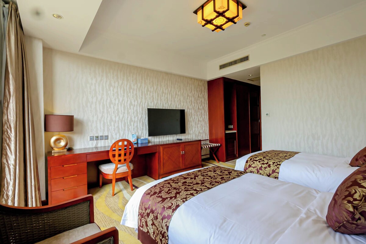 A hotel room with two beds, a desk with a TV, a chair, and a lamp.