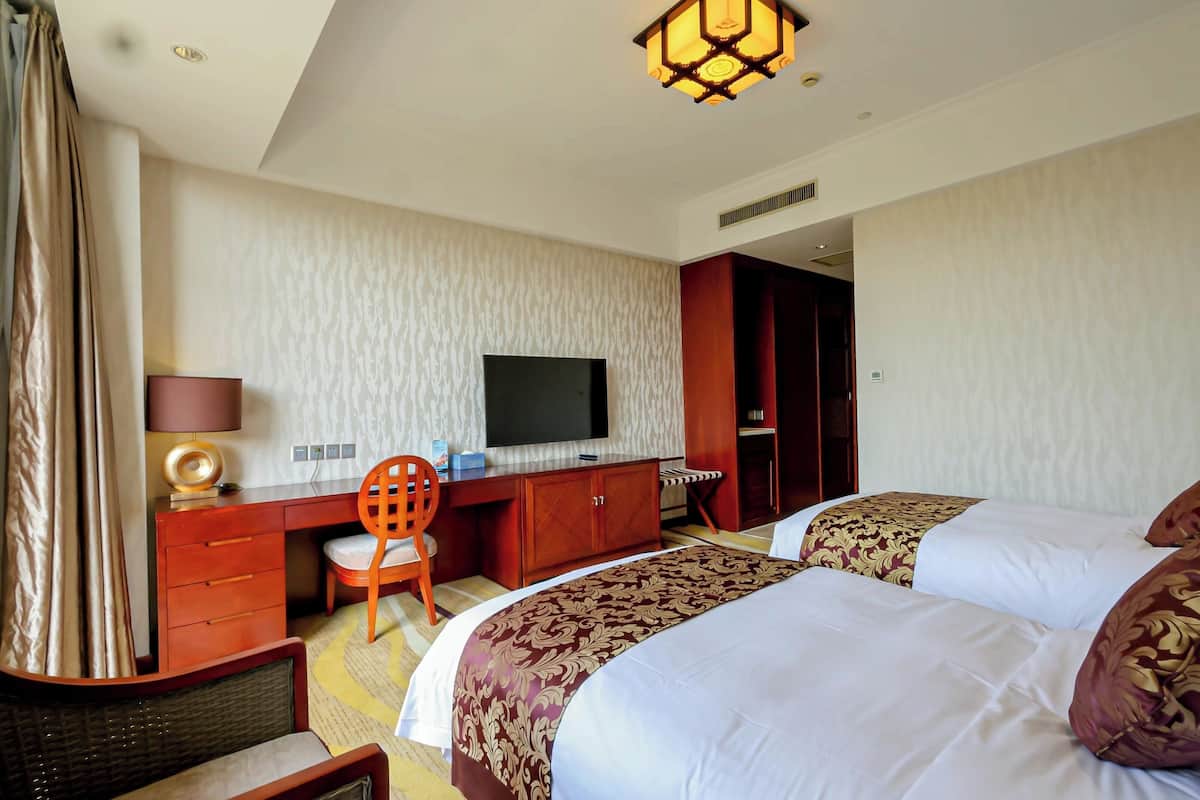 A hotel room with two beds, a desk with a TV, a chair, and a lamp.