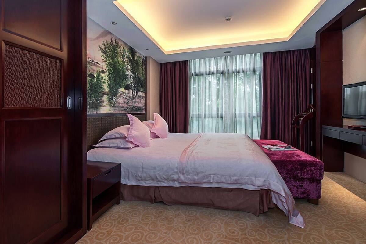 A hotel room with a large bed, a desk, a television, and a window with curtains.