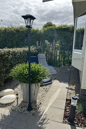 Un chemin de jardin bordé d’une plante en pot, d’un banc et d’un lampadaire.