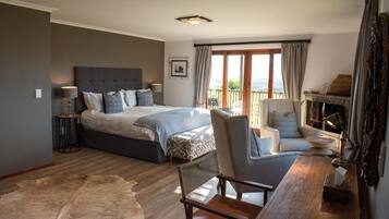 Ein Schlafzimmer mit einem großen Bett, einem Sessel, einem kleinen Tisch, einem Kamin und Blick ins Freie.