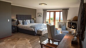 Une chambre avec un grand lit, une chaise, une petite table, une cheminée et une vue sur l’extérieur.