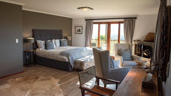 Ein Schlafzimmer mit einem großen Bett, einem Sessel, einem kleinen Tisch, einem Kamin und Blick ins Freie.