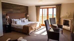 A spacious bedroom with a large bed, a sitting area with a fireplace, and a balcony with a scenic view. - Gondwana Game Reserve (Mossel Bay)