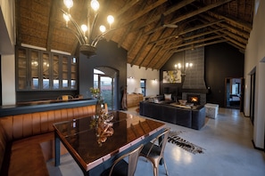 A spacious living area with a high ceiling, a fireplace, and a large dining table. - Gondwana Game Reserve (Mossel Bay)