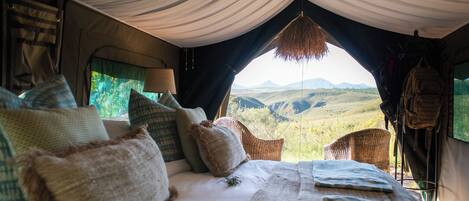 A tent with a bed, pillows, a hanging lamp, and a view of the landscape.