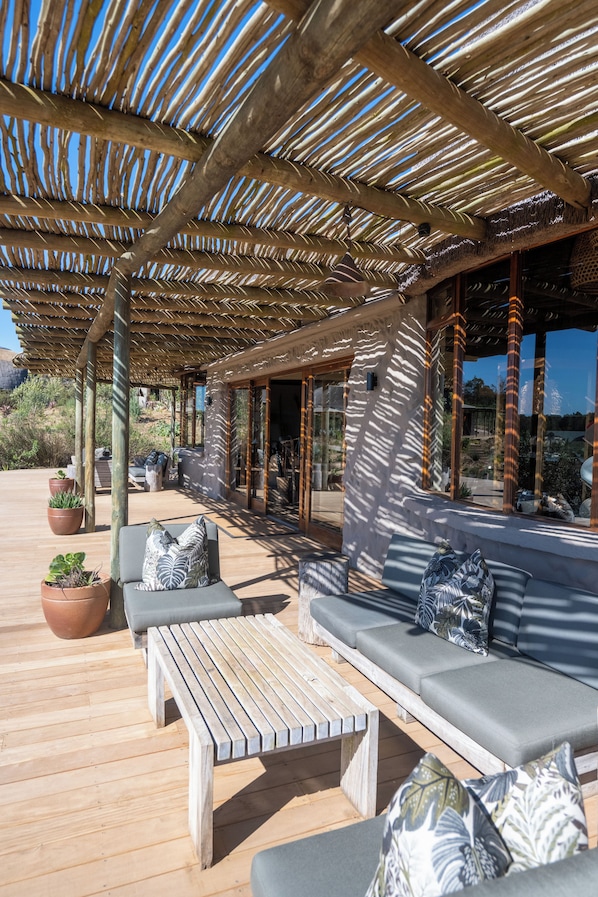 A covered outdoor seating area with wooden benches and cushions, potted plants, and a view of the surrounding landscape. - Gondwana Game Reserve (Mossel Bay)