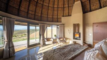 A spacious bedroom with a large bed, a fireplace, and a view of the countryside.