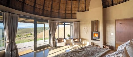 A spacious bedroom with a large bed, a fireplace, and a view of the countryside.