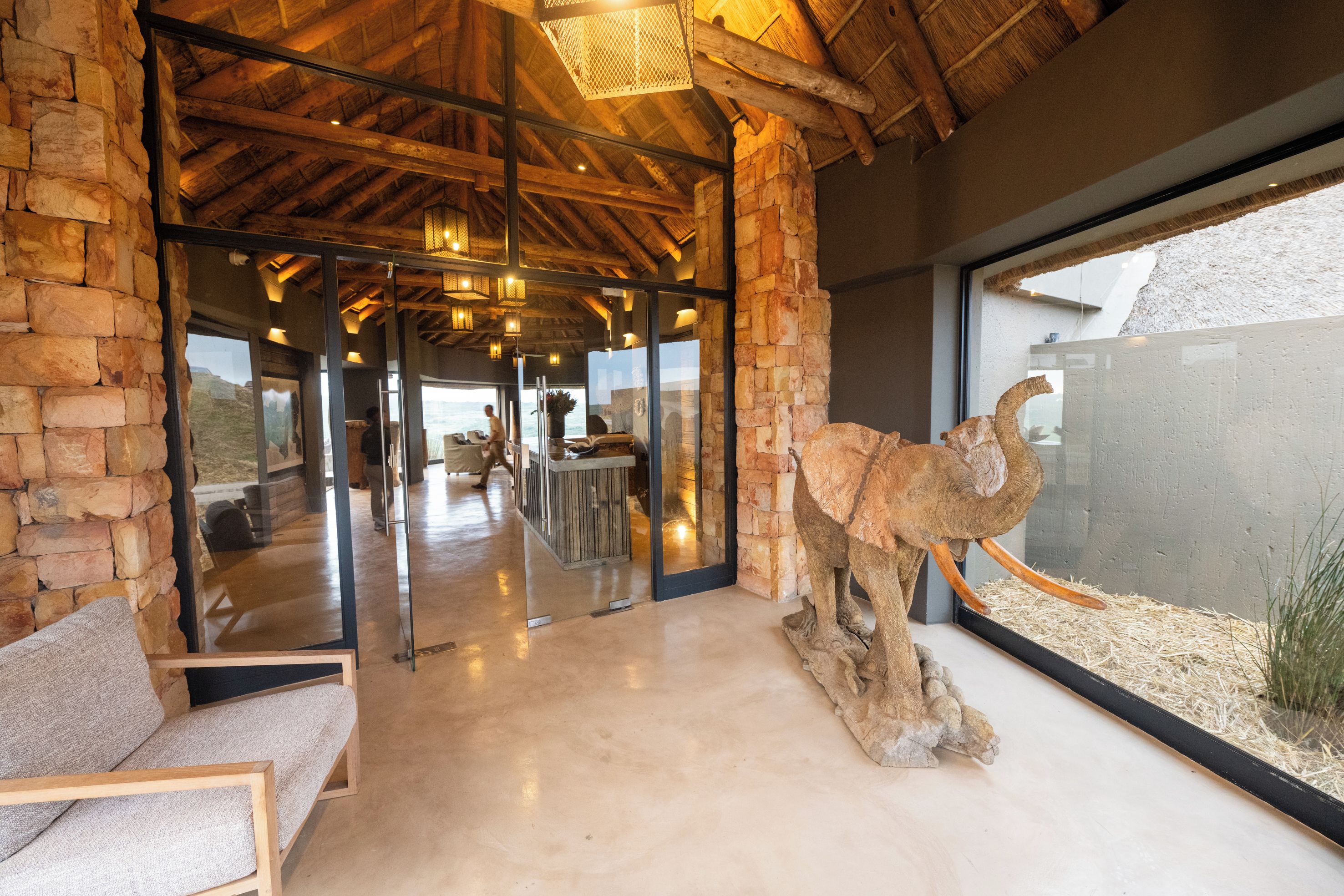 A modern interior with stone walls, wooden beams, a glass door leading outside, and a large animal sculpture.