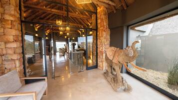 A modern interior with stone walls, wooden beams, a glass door leading outside, and a large animal sculpture.
