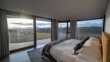 Une chambre avec un grand lit, une vue sur la campagne et une terrasse en bois à l’extérieur.