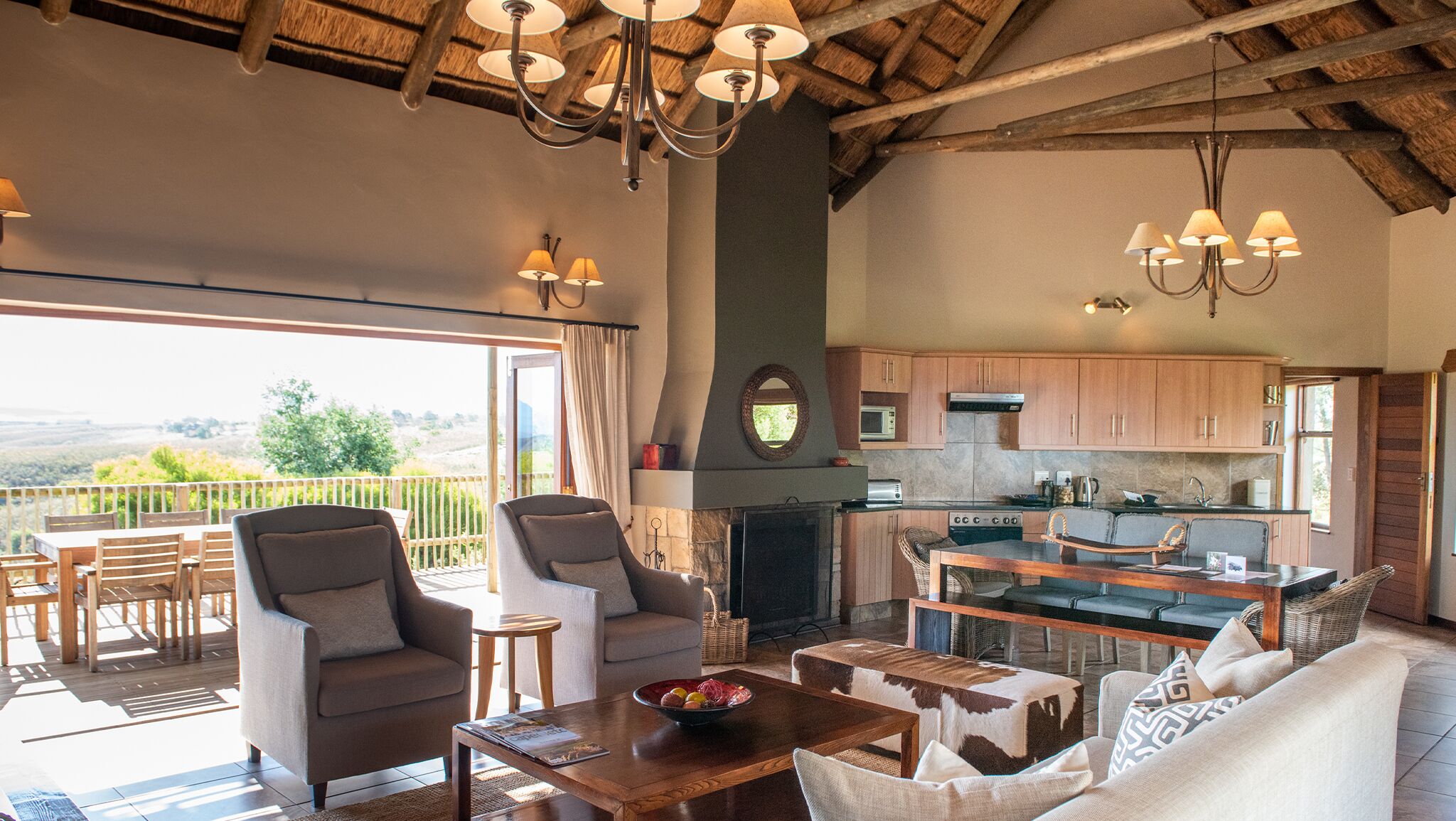 Amplia sala de estar con chimenea, mesa de comedor y asientos cómodos. Se observa una cocina con armarios de madera y electrodomésticos modernos al fondo.