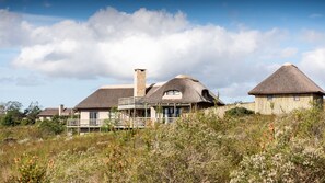 A thatched-roof house with a stone chimney, surrounded by natural vegetation. - Gondwana Game Reserve (Mossel Bay)