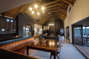 A spacious living area with a high ceiling, a fireplace, and a large dining table. - Gondwana Game Reserve (Mossel Bay)