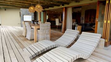 A wooden deck with lounge chairs, a wicker table, and a stone wall.