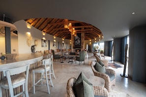 A spacious lounge area with a curved ceiling, wicker furniture, and a bar counter. - Gondwana Game Reserve (Mossel Bay)