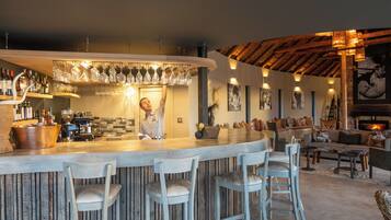 A bar area with a bartender, bar stools, a wooden ceiling, and a cozy seating area with cushions and a fireplace.