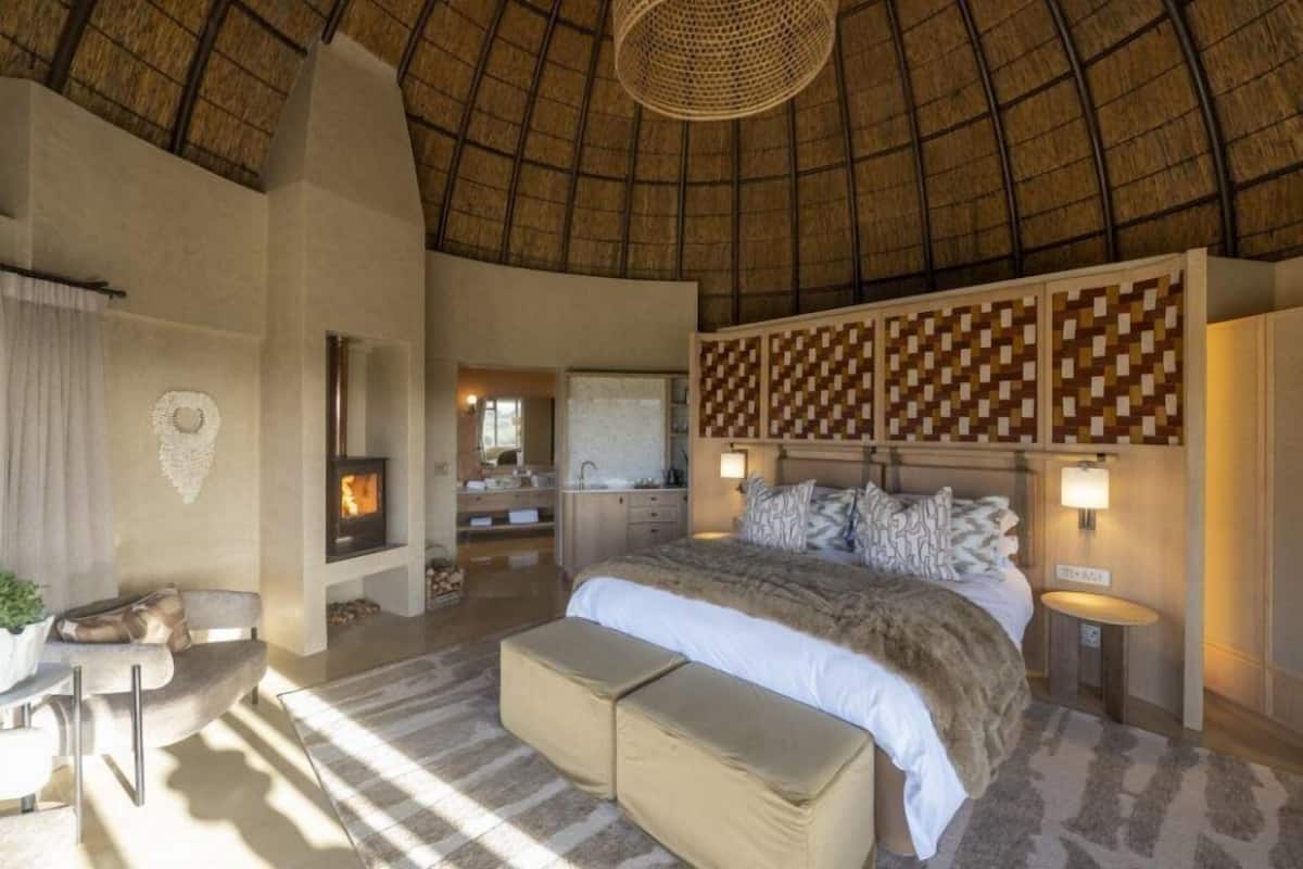 Un dormitorio con una cama grande, una chimenea, un techo de paja y vistas al baño.