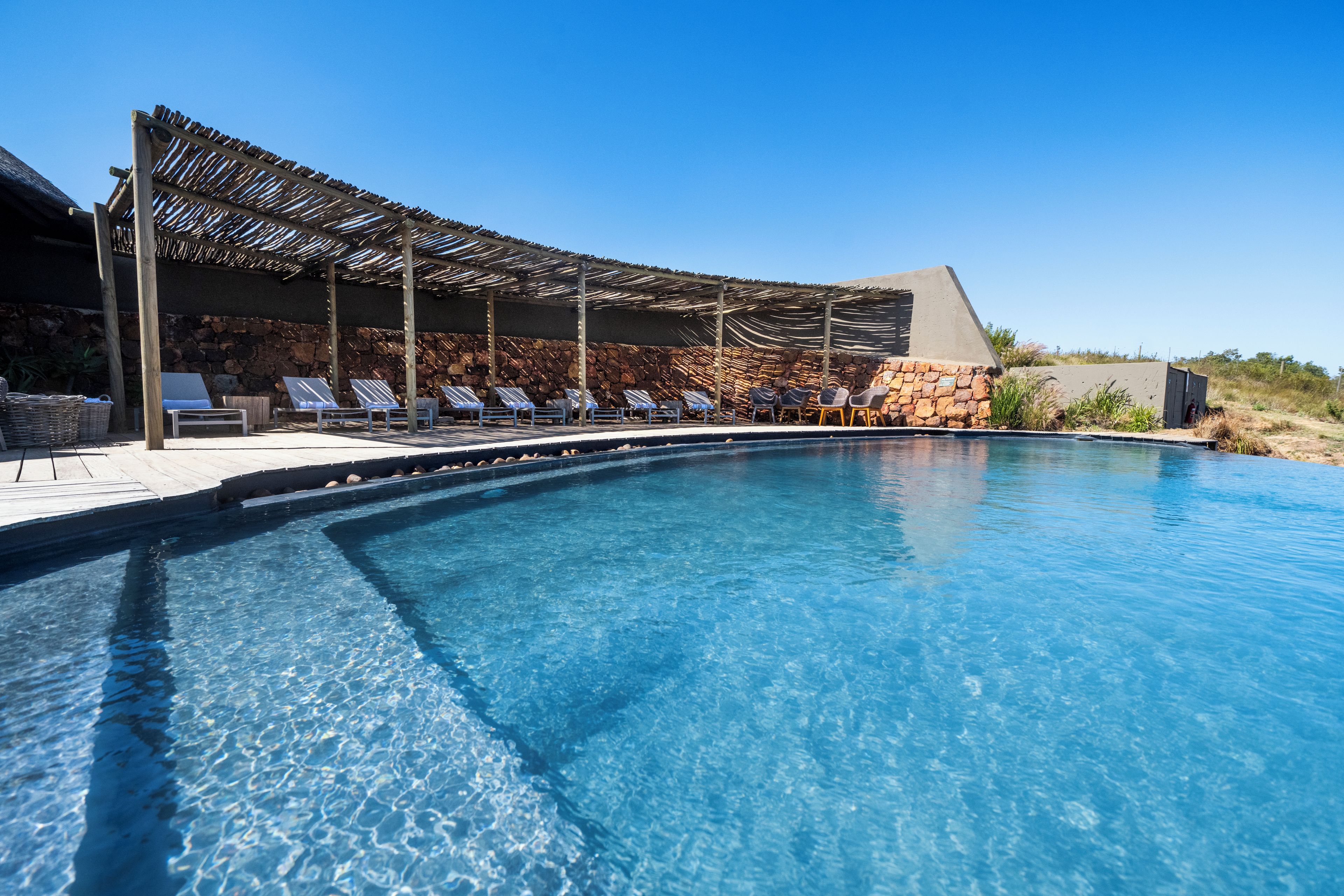 Une piscine aux eaux cristallines, dotée de chaises longues et d’une pergola.