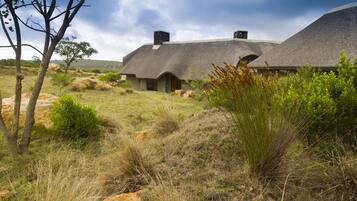 A thatched-roof house with a stone chimney, surrounded by natural vegetation and hills.