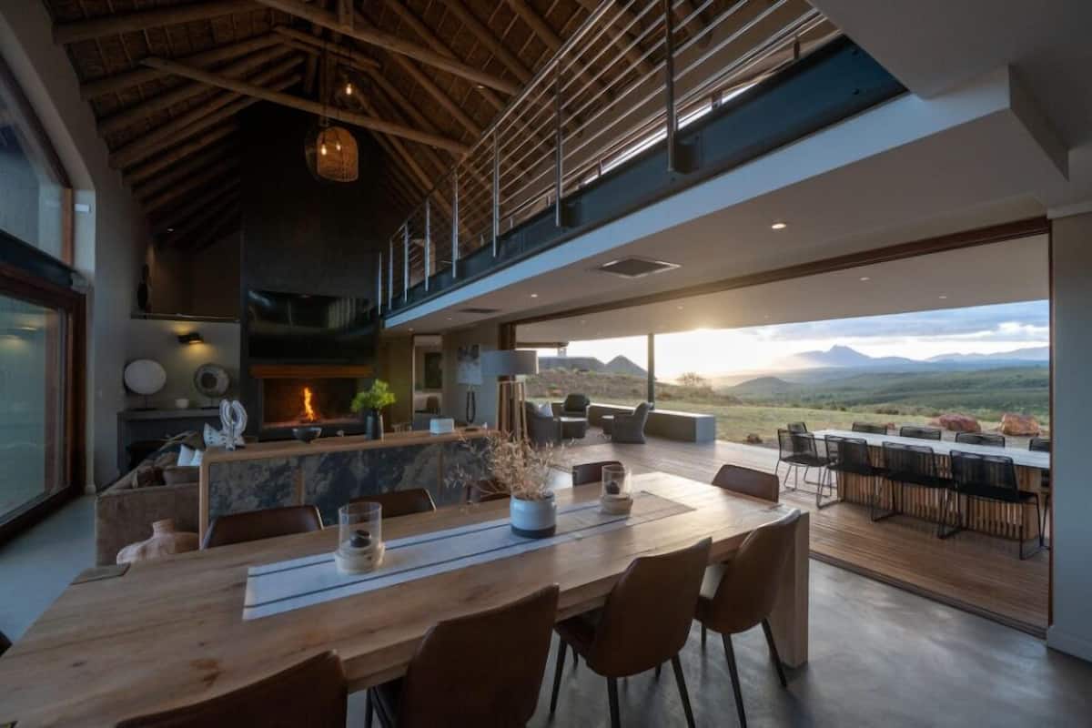 Un interior moderno con comedor, cocina y un amplio ventanal con vistas a un paisaje montañoso.