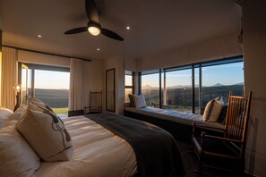 Ein Hotelzimmer mit einem großen Bett, einem Sessel, einer Sitzbank und Blick auf die Landschaft.