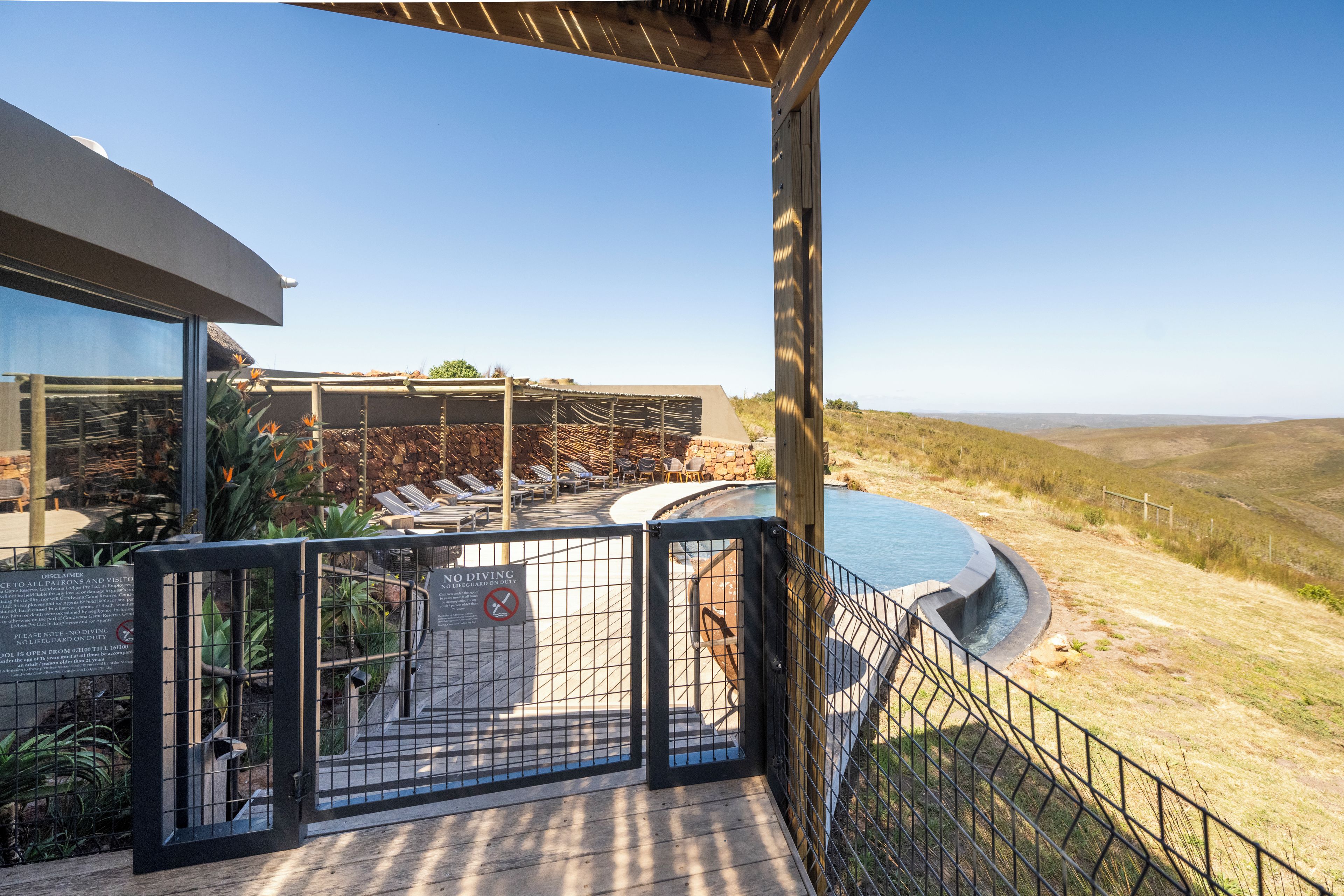 A pool with a surrounding deck, a clear sky, and a distant view of hills.