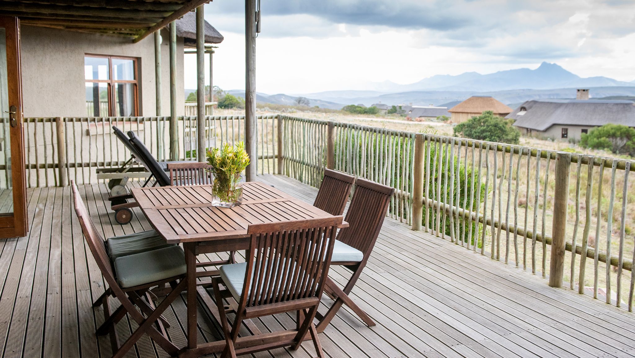Une terrasse en bois avec une table et des chaises, un pot de fleurs et une vue sur des montagnes lointaines.