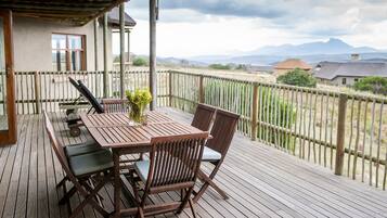 Une terrasse en bois avec une table et des chaises, un pot de fleurs et une vue sur des montagnes lointaines.