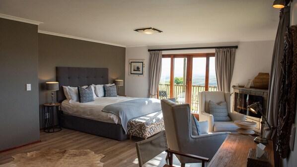 Une chambre à coucher avec un grand lit, une chaise, une petite table, une cheminée et un balcon avec des rideaux.