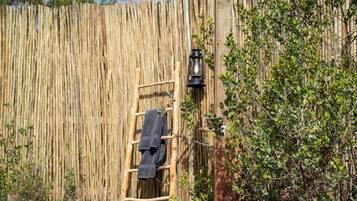Une terrasse en bois menant à une porte en bois, une serviette suspendue à une échelle en bois et un lampadaire.