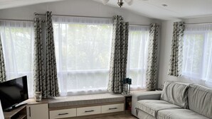 Ein stilvolles Wohnzimmer mit Sofa, Fernseher, Esstisch und Fenstern mit Vorhängen.