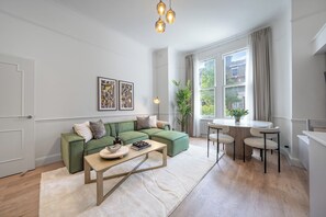 Ein modernes Wohnzimmer mit einem grünen Sofa, einem Holztisch und einem Essbereich mit kleinem Tisch und Stühlen.