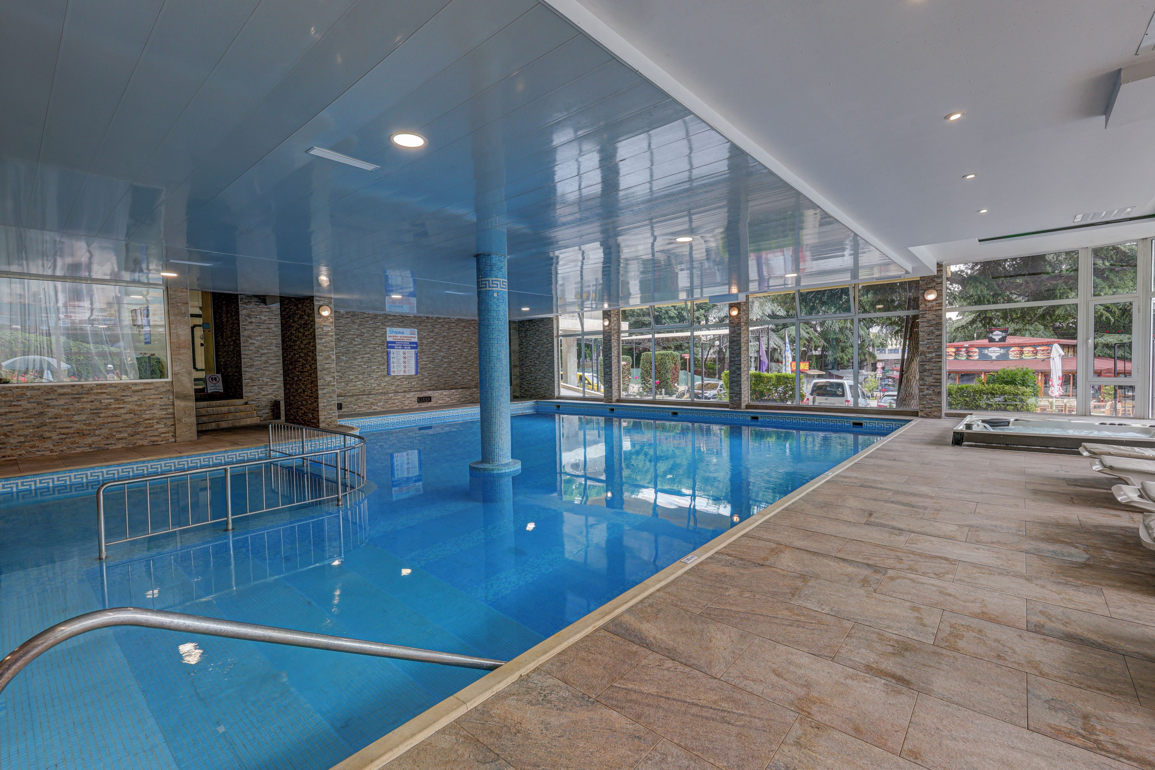 An indoor swimming pool with clear glass walls, a tiled floor, and a pool ladder.