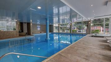 An indoor swimming pool with clear glass walls, a tiled floor, and a pool ladder.