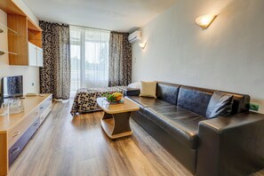 A modern living room with a sofa, a coffee table, a TV, and a dining area with a table and chairs. - Hotel Shipka All Inclusive (Varna)